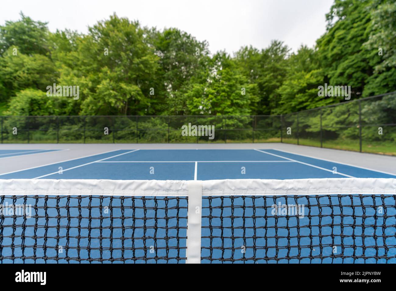 Over the net view of a new blue tennis court with white lines and gray