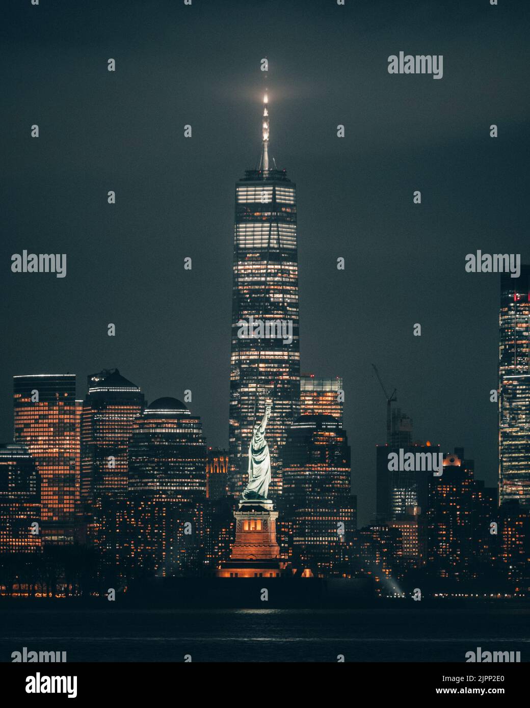 A vertical shot of the Statue of Liberty and skyscrapers at night in New York, United States Stock Photo