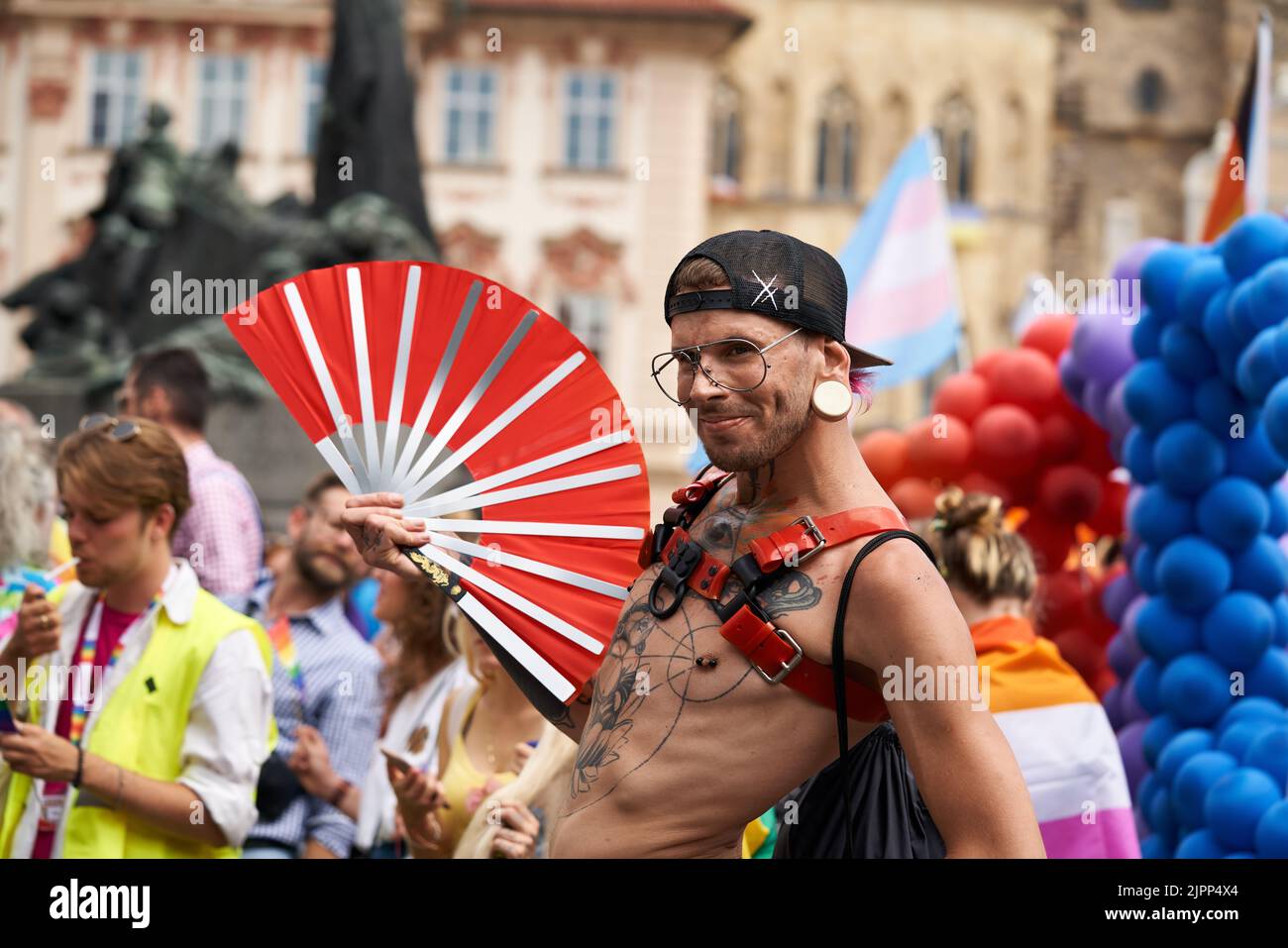 PRAGUE, CZECH REPUBLIC - AUGUST 13, 2022: Extravagant LGBT man with red fan posing at the Old Town Square during gay pride Stock Photo