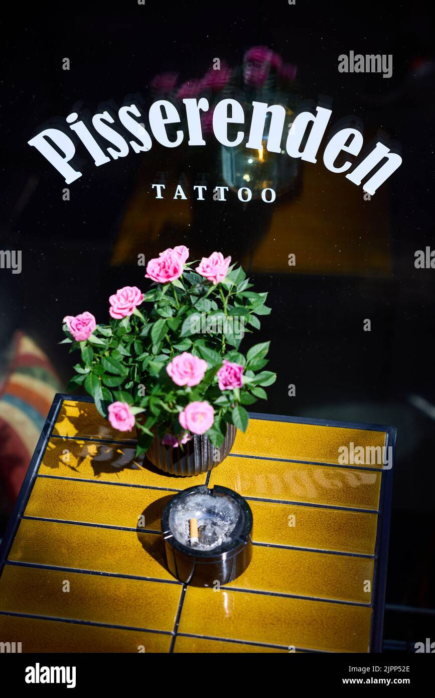 Pisserenden Tattoo, sign on window, pink roses and ashtray on tile-topped table; Copenhagen, Denmark Stock Photo