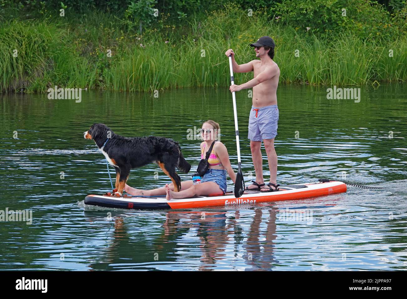 A young couple and their dog ride a standup paddleboard on the Dewschutes River in Bend, Oregon. Stock Photo