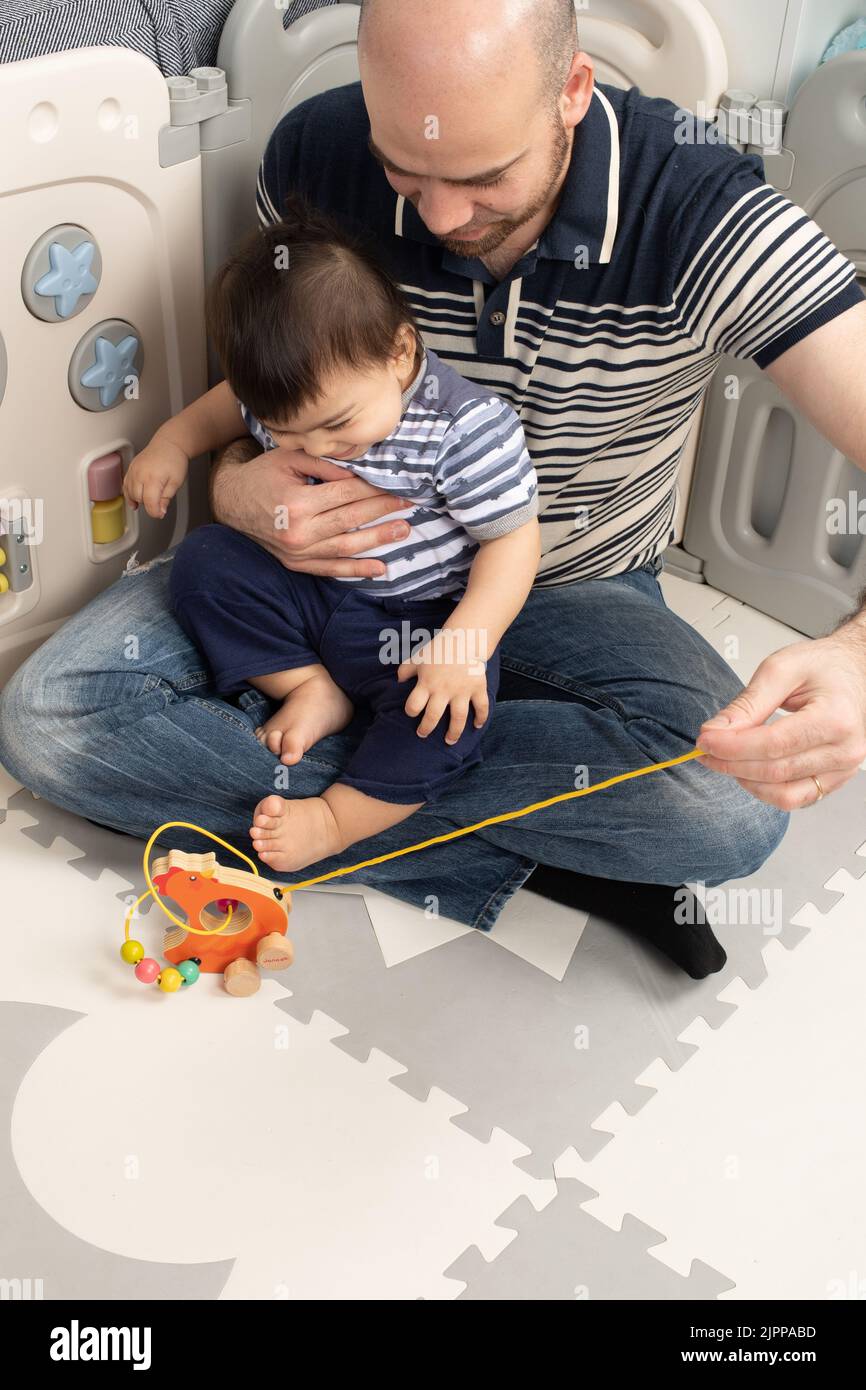 11 month old baby boy at home with father shown how pulling a string brings a wheeled toy closer Stock Photo