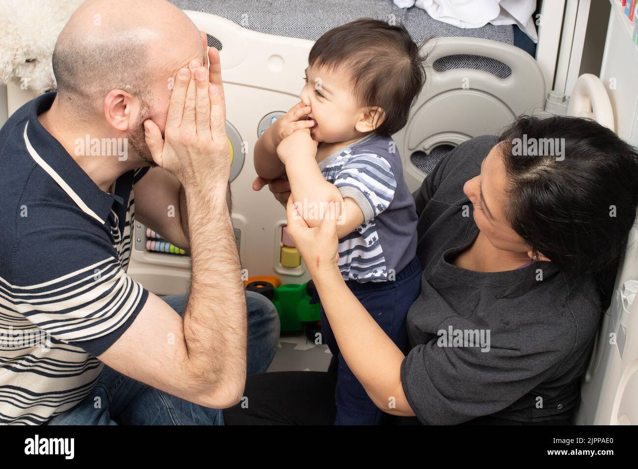 11 month old baby boy at home playing peek a boo with parents Stock Photo