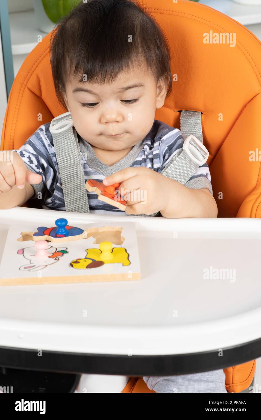 11 month old baby in high chair playing with puzzle picking up piece using pincer grasp Stock Photo