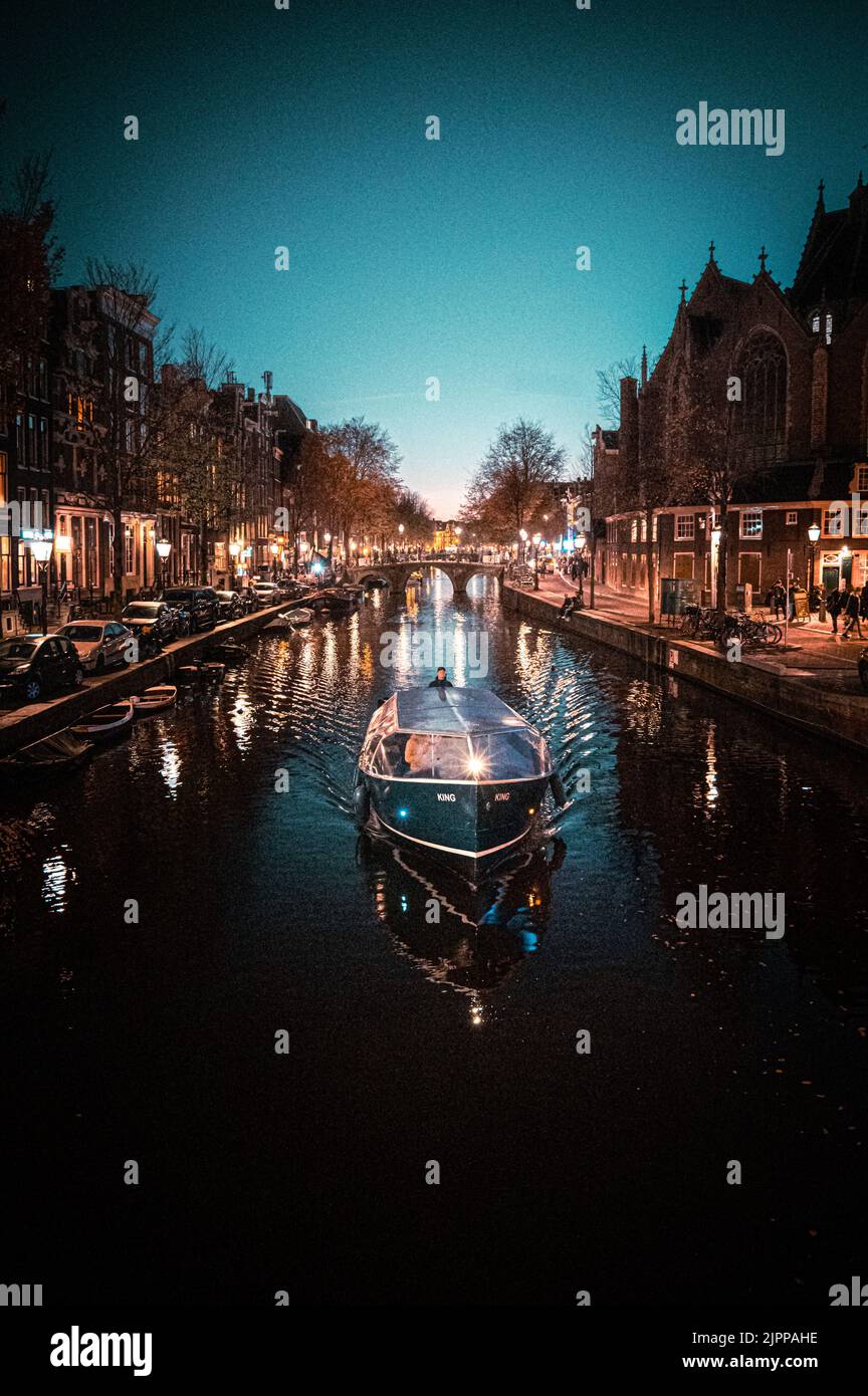 A vintage canal boat sailing down a narrow canal at night with
