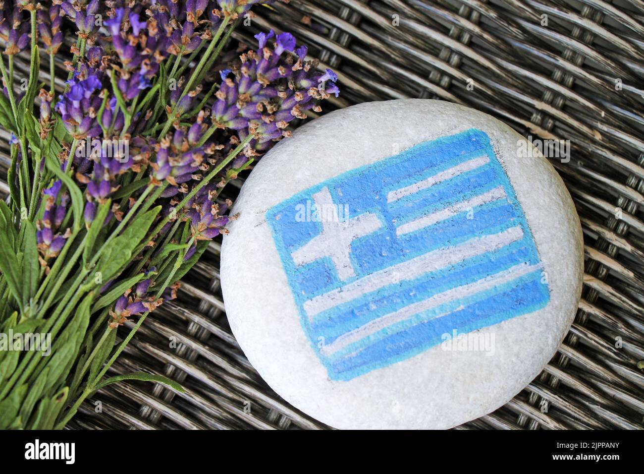 Greece country flag painted on the stones with bunch of fresh lavender flowers on wicker desk background. Stock Photo