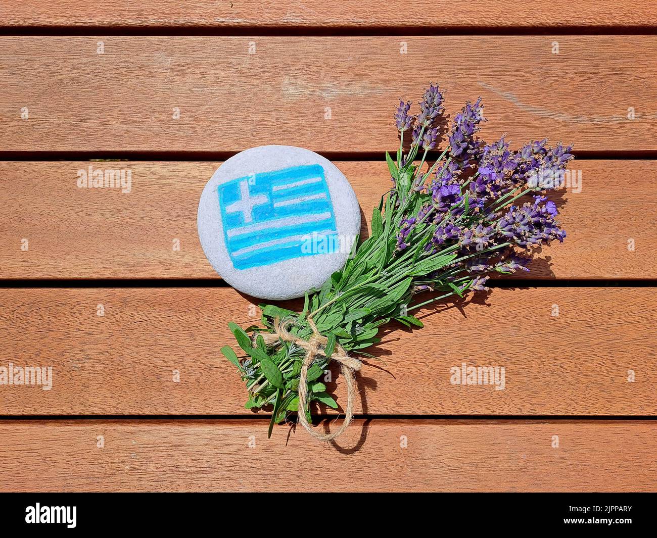 Greece country flag painted on the sea stone with bunch of fresh lavender flowers on wooden plank background. Stock Photo