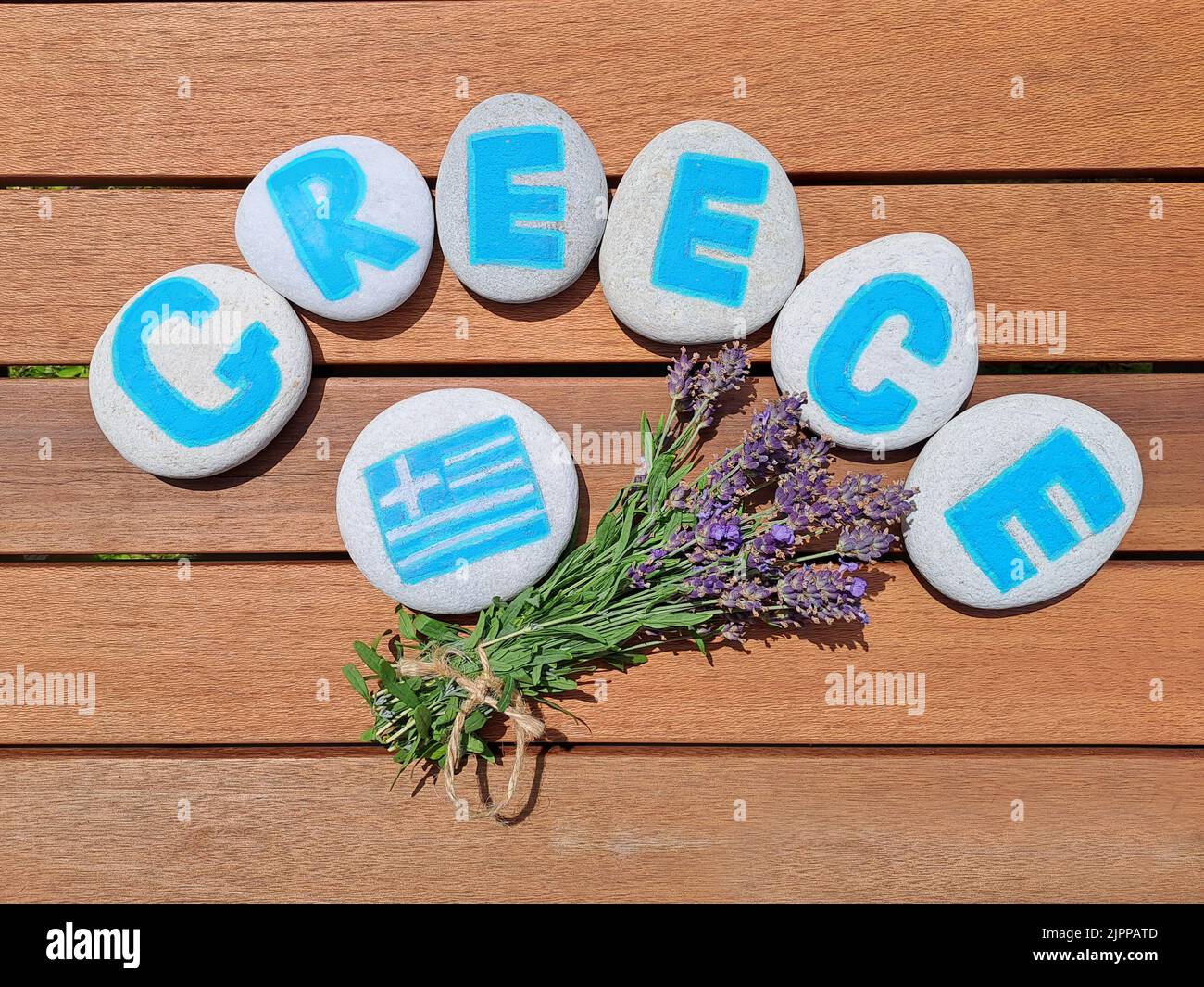Greece country name painted on the stones with bunch of fresh lavender flowerson wooden plank background. Inskription on the sea stones. Stock Photo