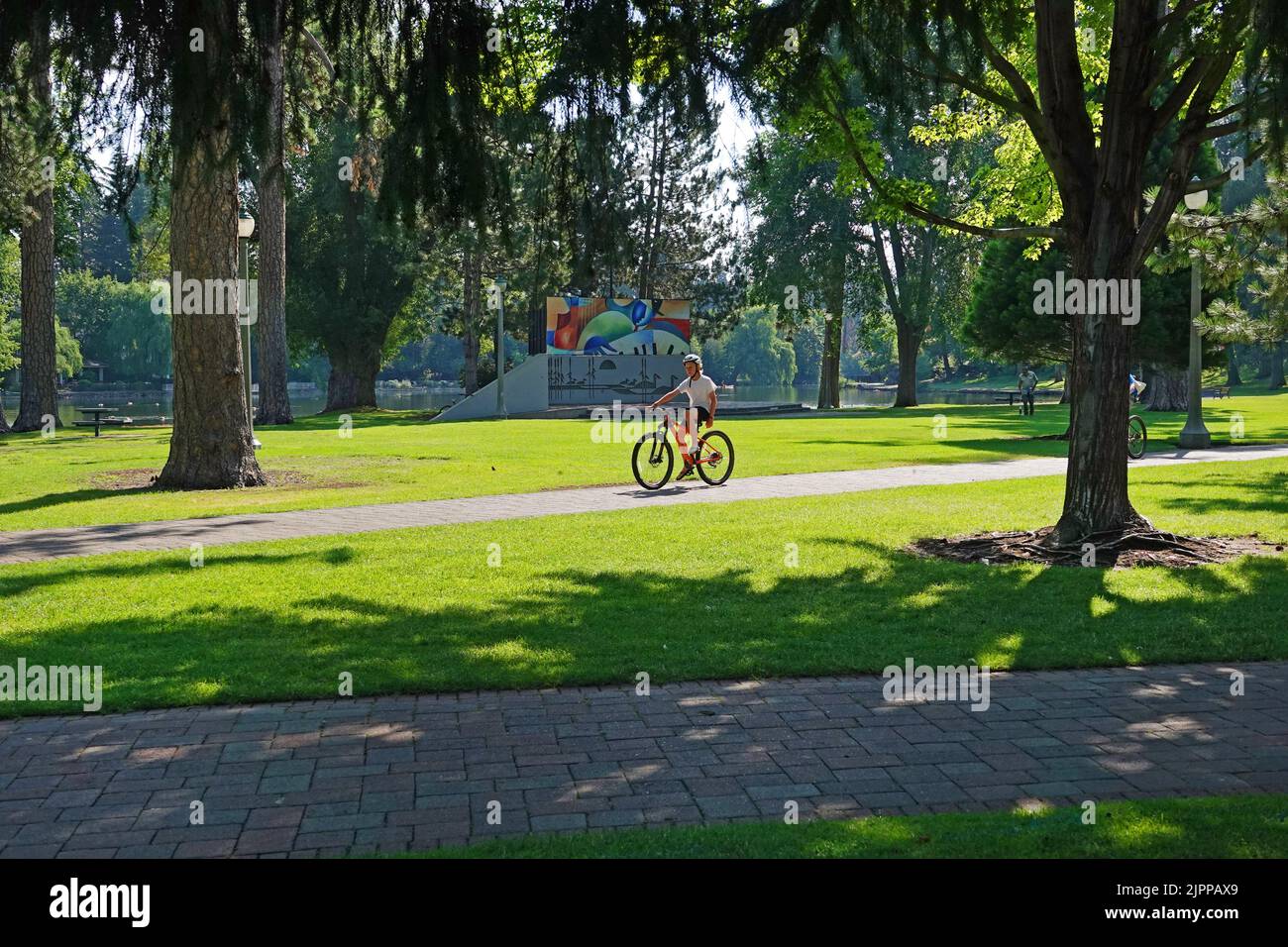 A boy riding a bicycle along a sidewalk in Drake Park along the Deschutes River in Bend, Oregon. Stock Photo