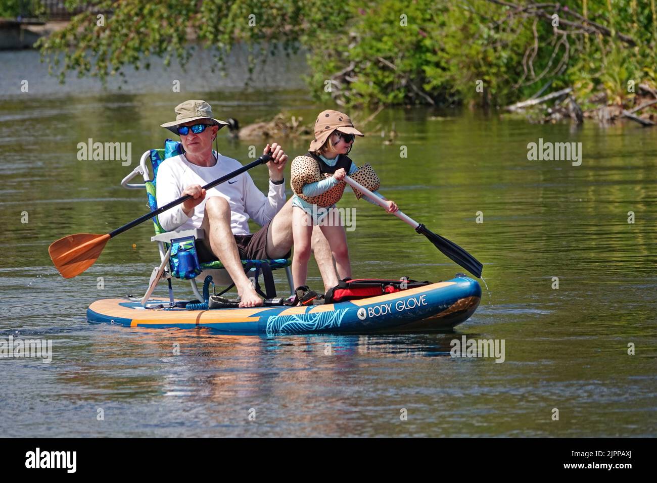 Grandpa and granddaughter float the Deschutes River in Bend, Oregon, on a paddleboard trying to escape the 100 degree F heatwave that is sweeping the Pacific Northwest. Stock Photo