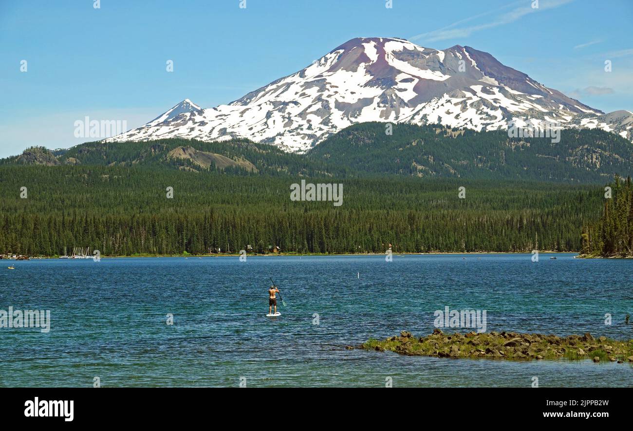 A standup paddleboarder on Elk Lake in the central Oregon Cascade Mountains along the Cascade Lake Highway. South Sisters Peak in the three Sisters Wilderness Area is in the background. Stock Photo