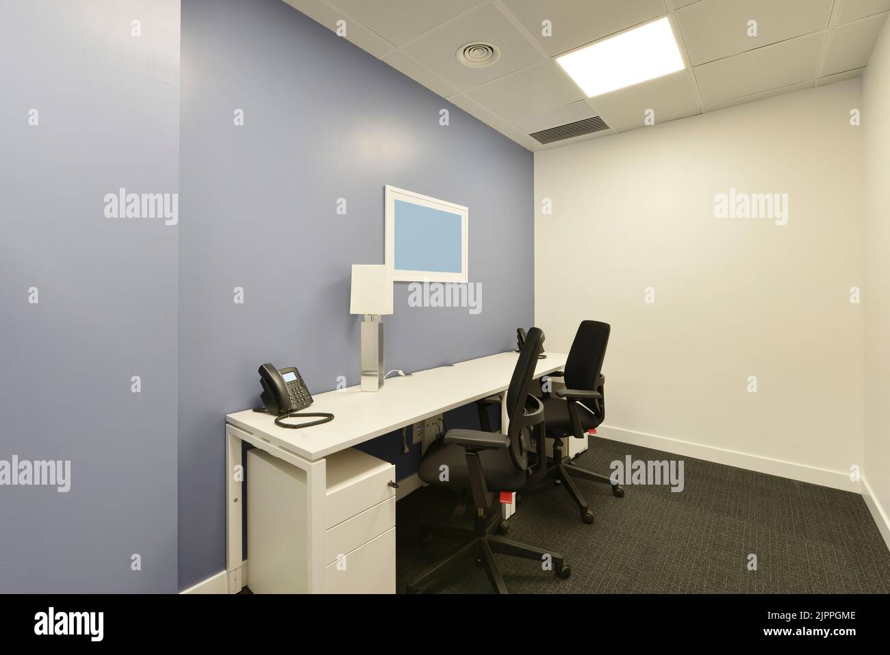 Small office cubicle with a white table, two chests of drawers, two ...