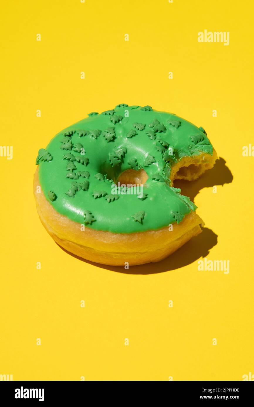 A vertical shot of a bitten donut with green frosting and sprinkles on ...