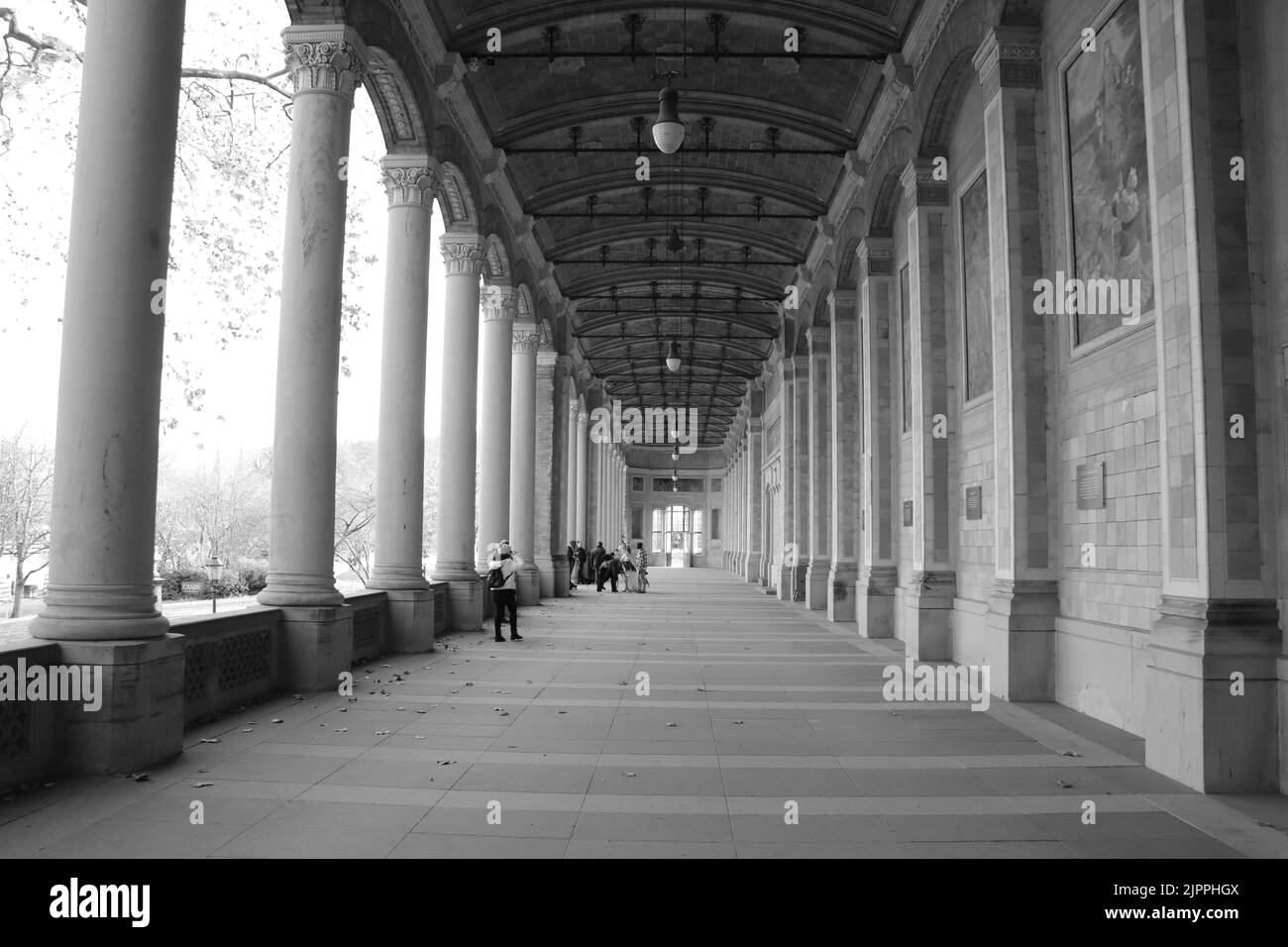 The main corridor of the Trinkhalle building with religious art pieces on walls and columns in grayscale Stock Photo