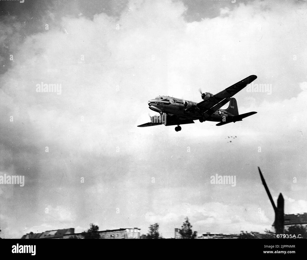 C-54 dropping candy during Berlin Airlift, circa 1949. A U.S. Air Force Douglas C-54 Skymaster making a 'Little Vittles' candy drop (note the parachutes below the tail of the C-54) on approach to a Berlin airfield. Aircrews dropped candy to children during the Berlin Airlift. Stock Photo