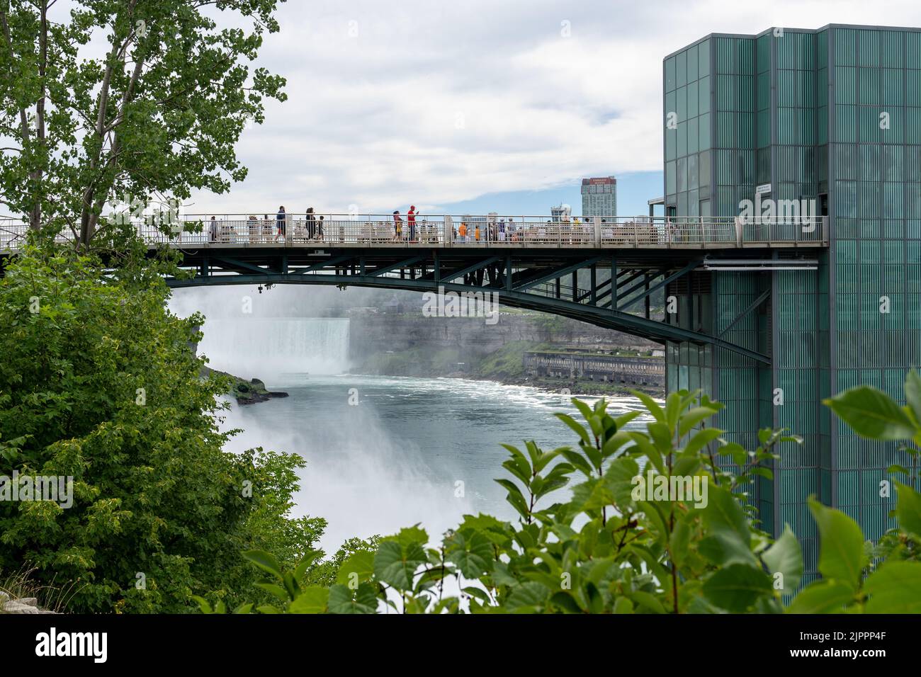 Niagara Falls, NY - July 31, 2022: View of Niagara Falls shrowded in mist, framed by the bridge leading to the observation deck and trees. Stock Photo