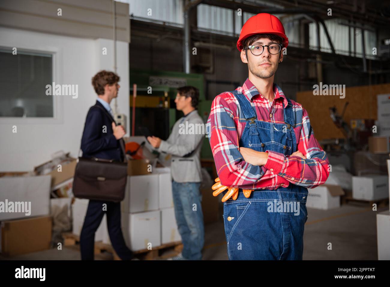 portrait of a factory worker with managers in the background discussing Stock Photo