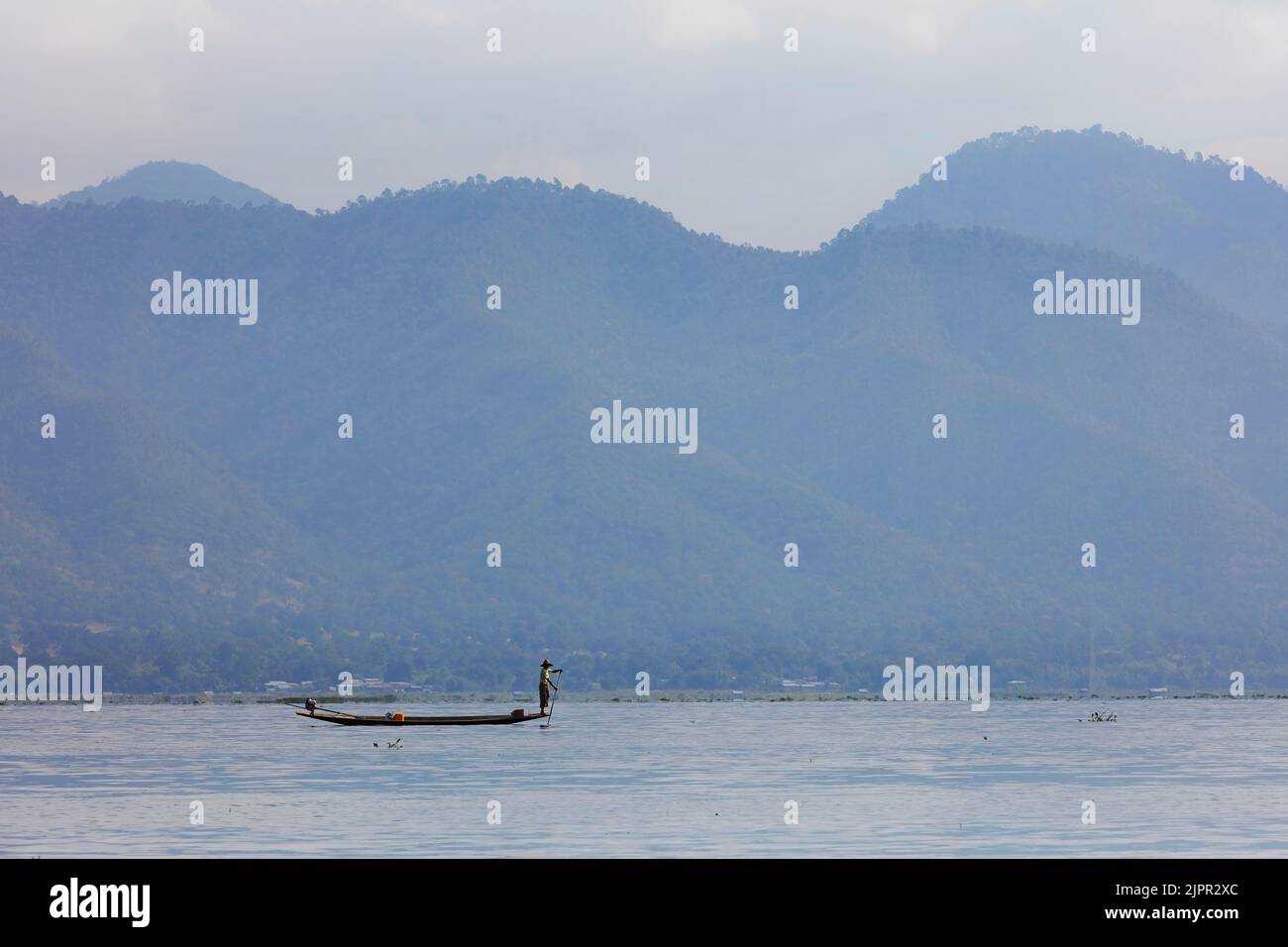 A traditional Intha Burmese One-Legged fisherman on his wooden boat with the mountains in the background, Inle Lake, Myanmar. Stock Photo
