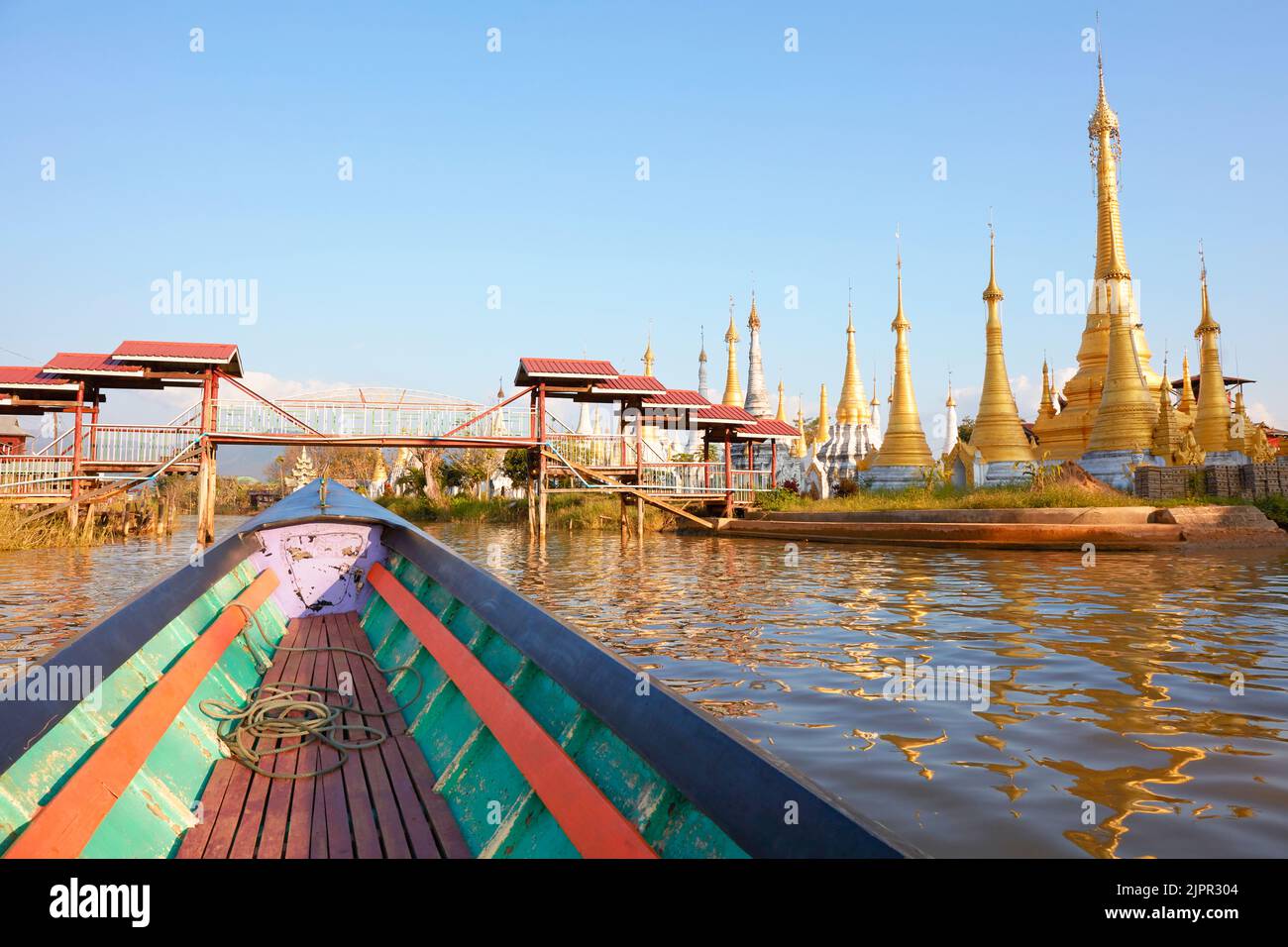 A wooden boat navigates on Inle Lak with golden Buddhist Pagodas in the background, Myanmar. Stock Photo