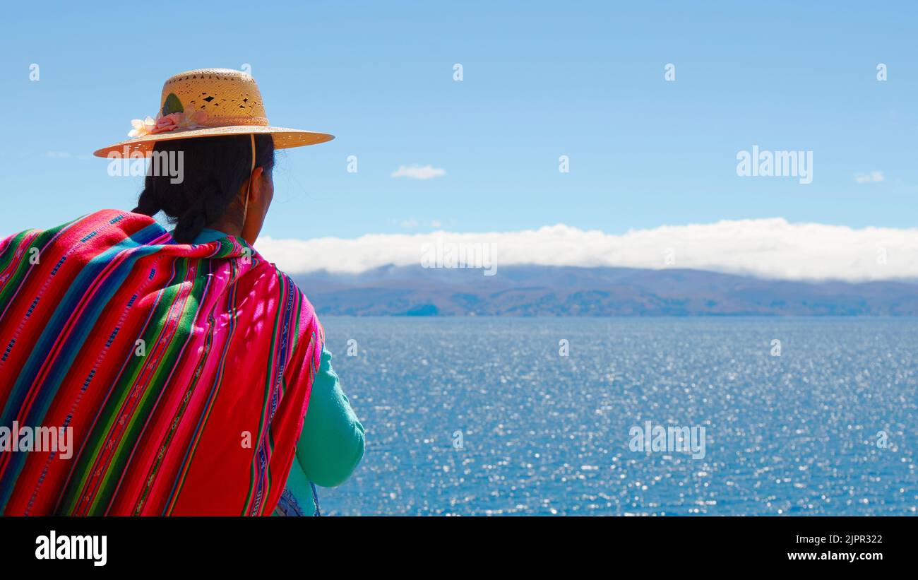 A Bolivian 'chola' woman in traditional colorful clothes looking at the horizon on the 'Isla de la Luna' on Lake Titicaca, La Paz province, Bolivia. Stock Photo
