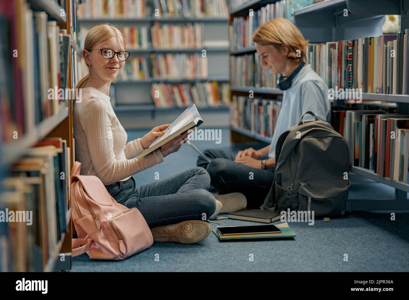 Friends student sit on floor near bookshelves in library and studying. Prepearing for exam Stock Photo