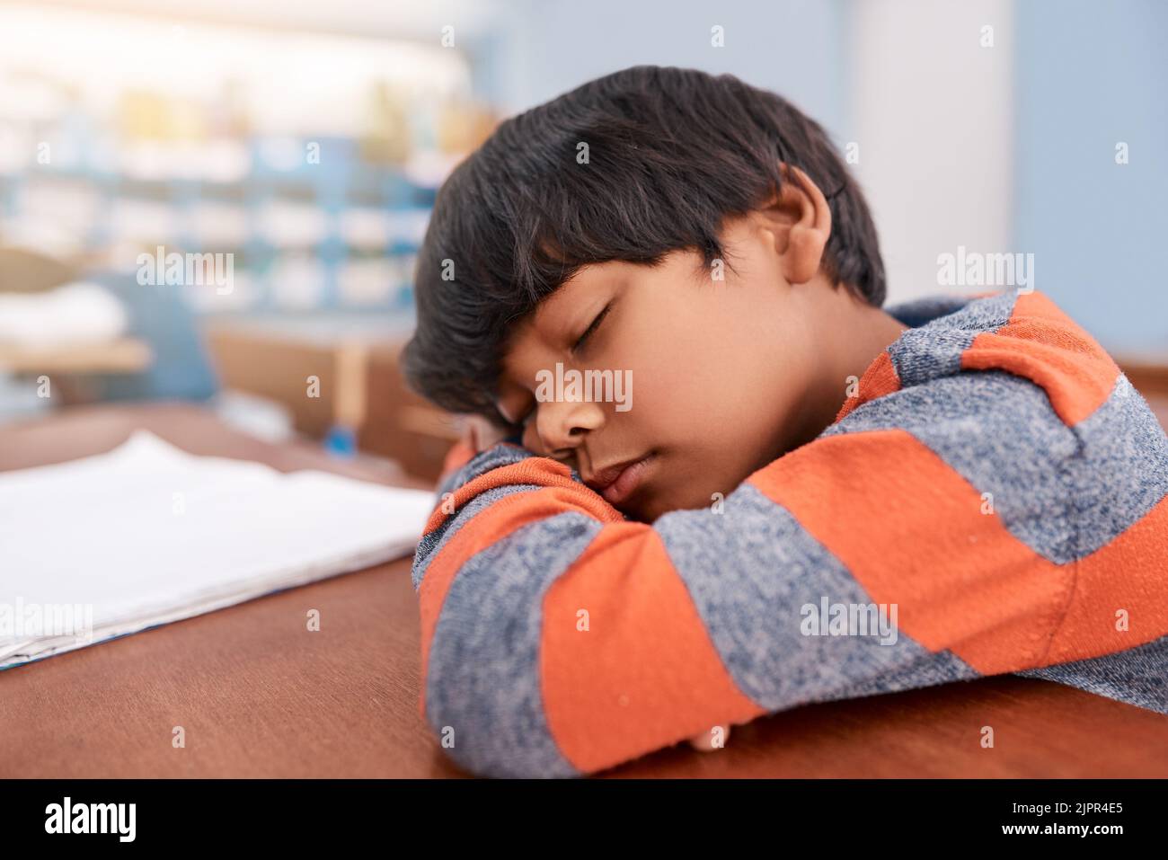 Just a quick nap. a tired elementary school child sleeping on his desk in the classroom. Stock Photo