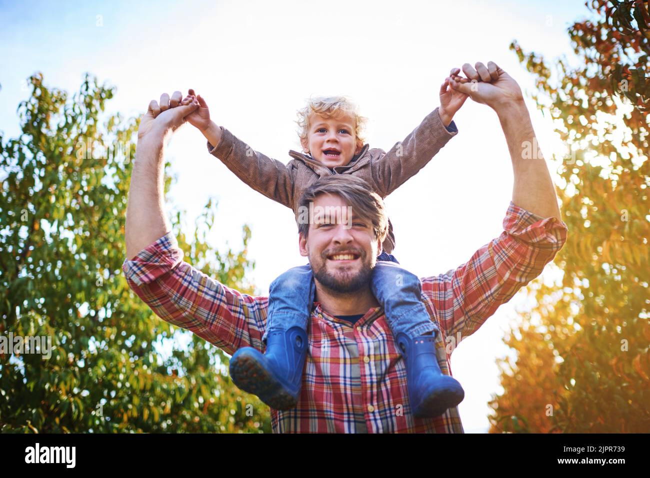 Hes my little champion. Low angle portrait of a handsome young man piggybacking his son outside during autumn. Stock Photo