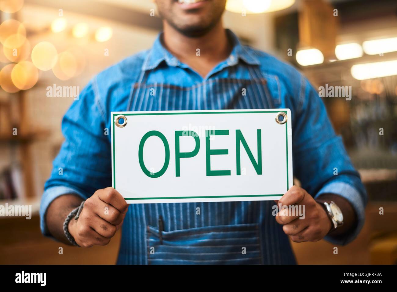 Open for business. Closeup shot of an unrecognizable man holding up an open sign in his store. Stock Photo
