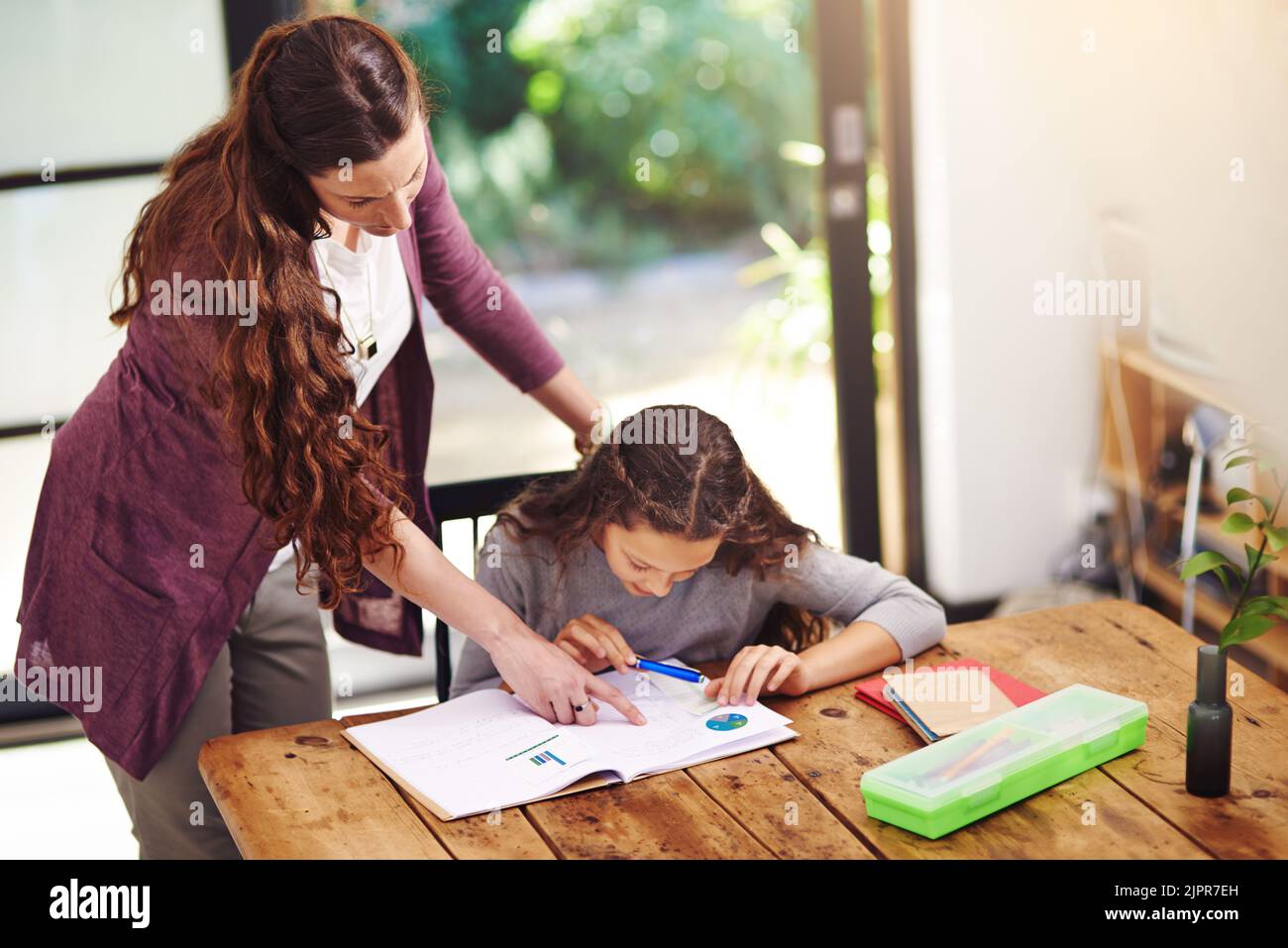 Read that to me. a young girl doing homework with her mother inside. Stock Photo