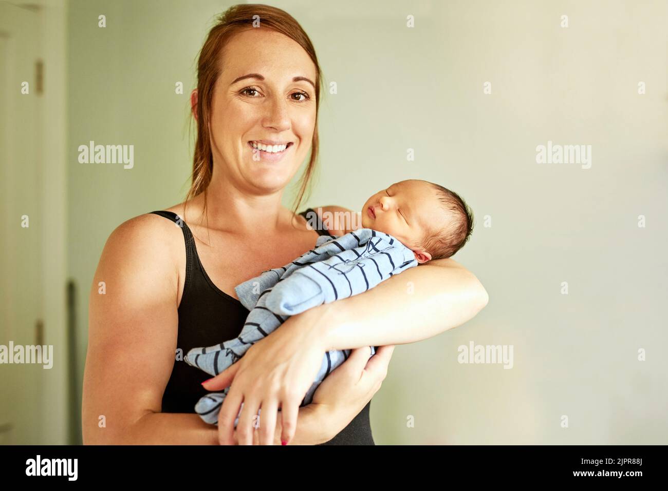 Shhh hes asleep. Portrait of cheerful young mother holding her infant son while looking into the camera at home. Stock Photo