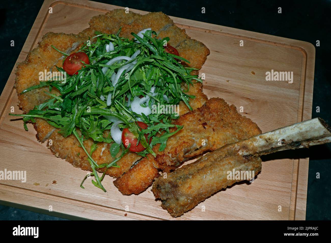 Veal Milanese, or veal alla Milanese, is an Italian popular dish,traditionally prepared with a veal rib chop or sirloin bone-in and made into a breade Stock Photo