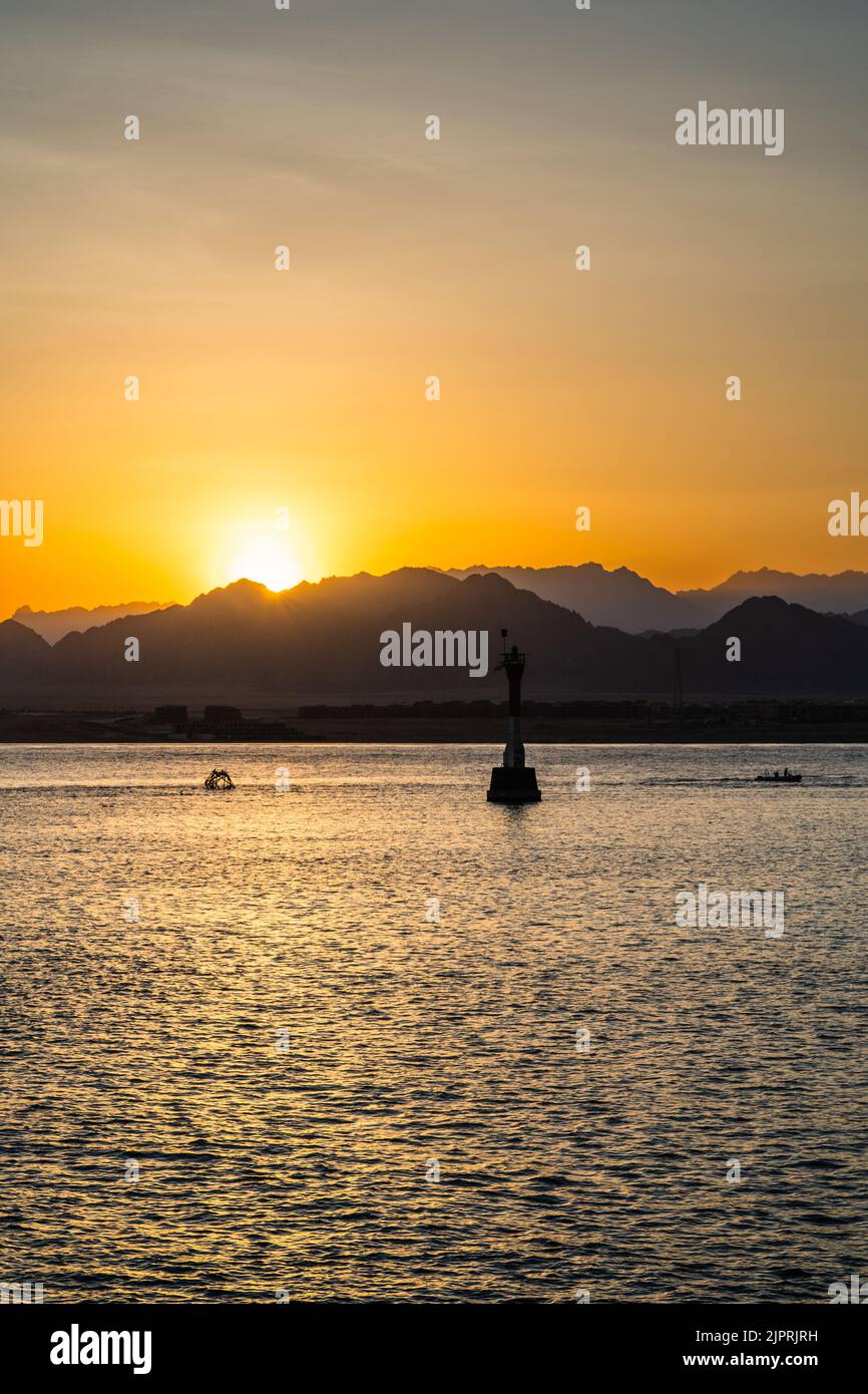 Picturesque sunset from dive boat on the sea with small lighthouse silhouette and mountains visible at Straits of Tiran near Sharm-El-Sheikh, Egypt. Stock Photo