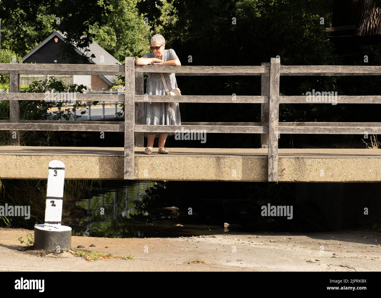Lady standing on a bridge in Brockenhurst, New Forest looking down on a dried up Ford and water depth marker in a drought Stock Photo