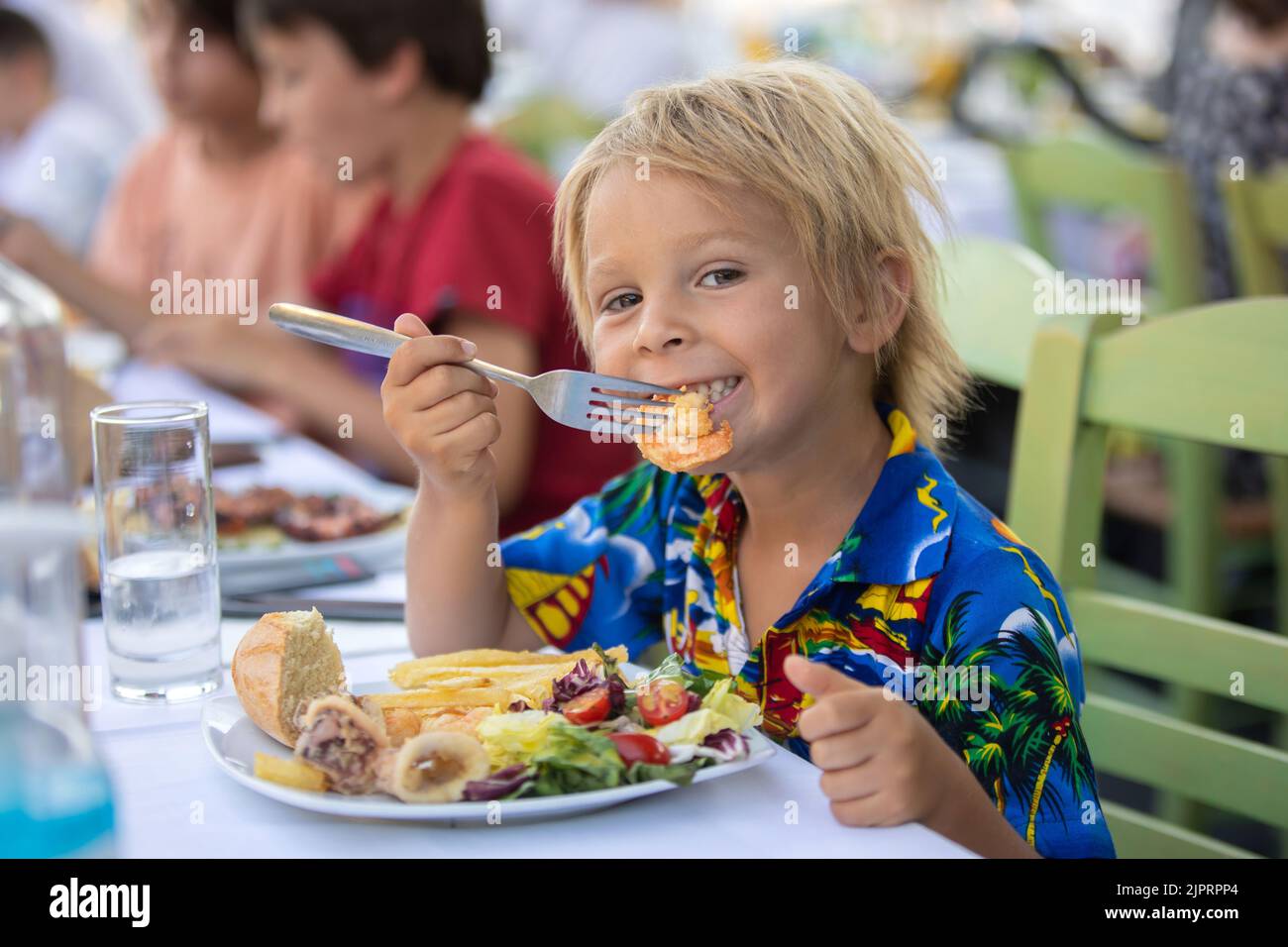 Sweet child, sitting in restaurant summertime outdoor, eating seafood, shrimps, calamari