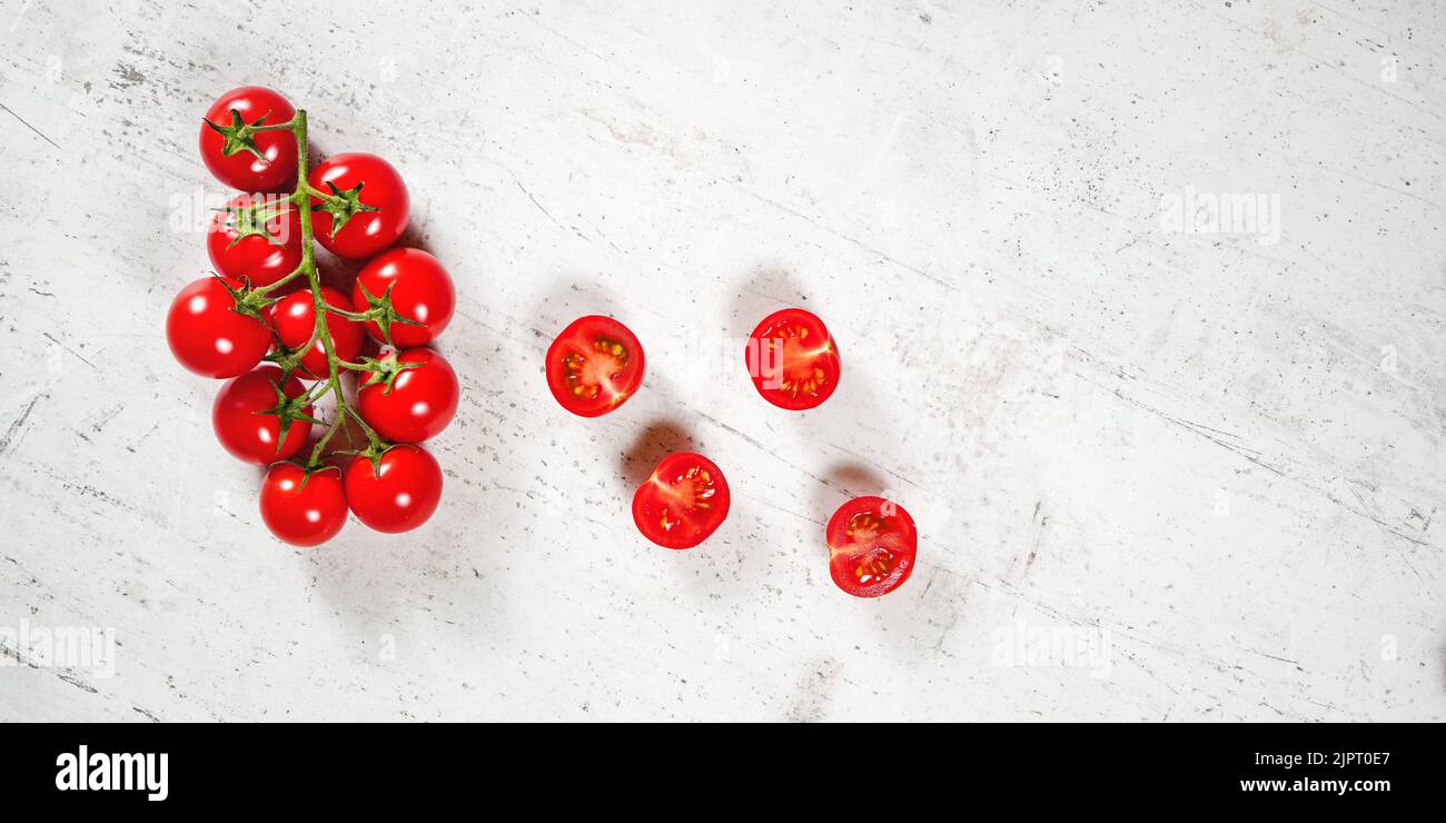 Vibrant small red tomatoes with green vines on white stone like board, view from above, empty space for text right side Stock Photo