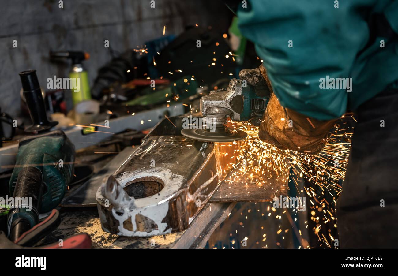 Man working with rotary angle grinder at workshop, closeup detail, orange sparks flying around Stock Photo