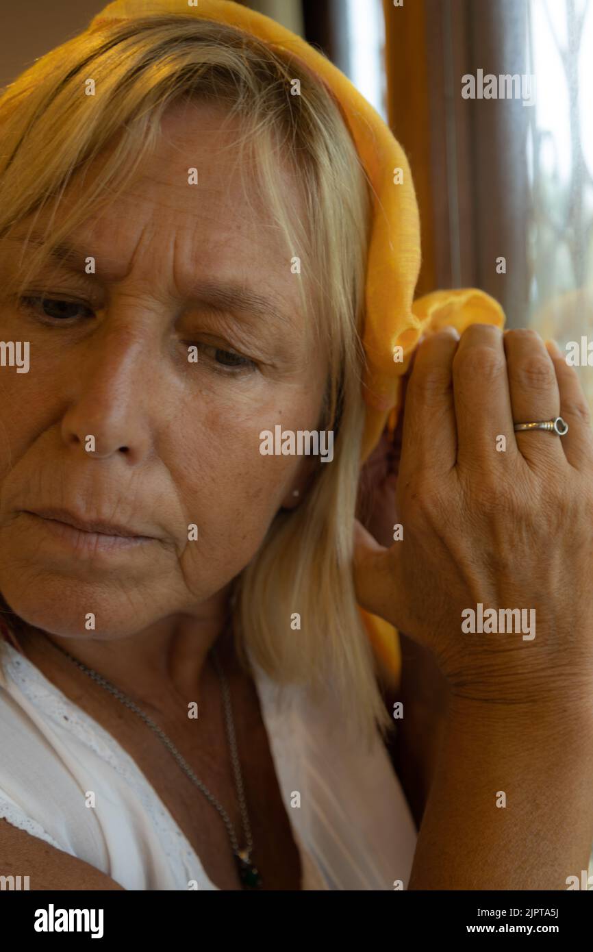 white woman in her 50s listening from behind a window with a worried face. Stock Photo