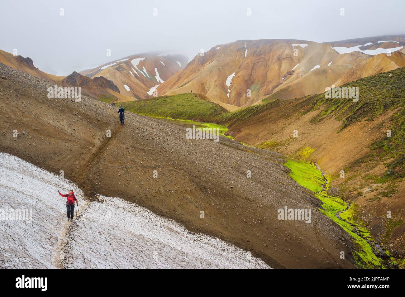 A high-angle shot of people walking across snow field in Landmannalaugar mountain range in Iceland on a misty day Stock Photo