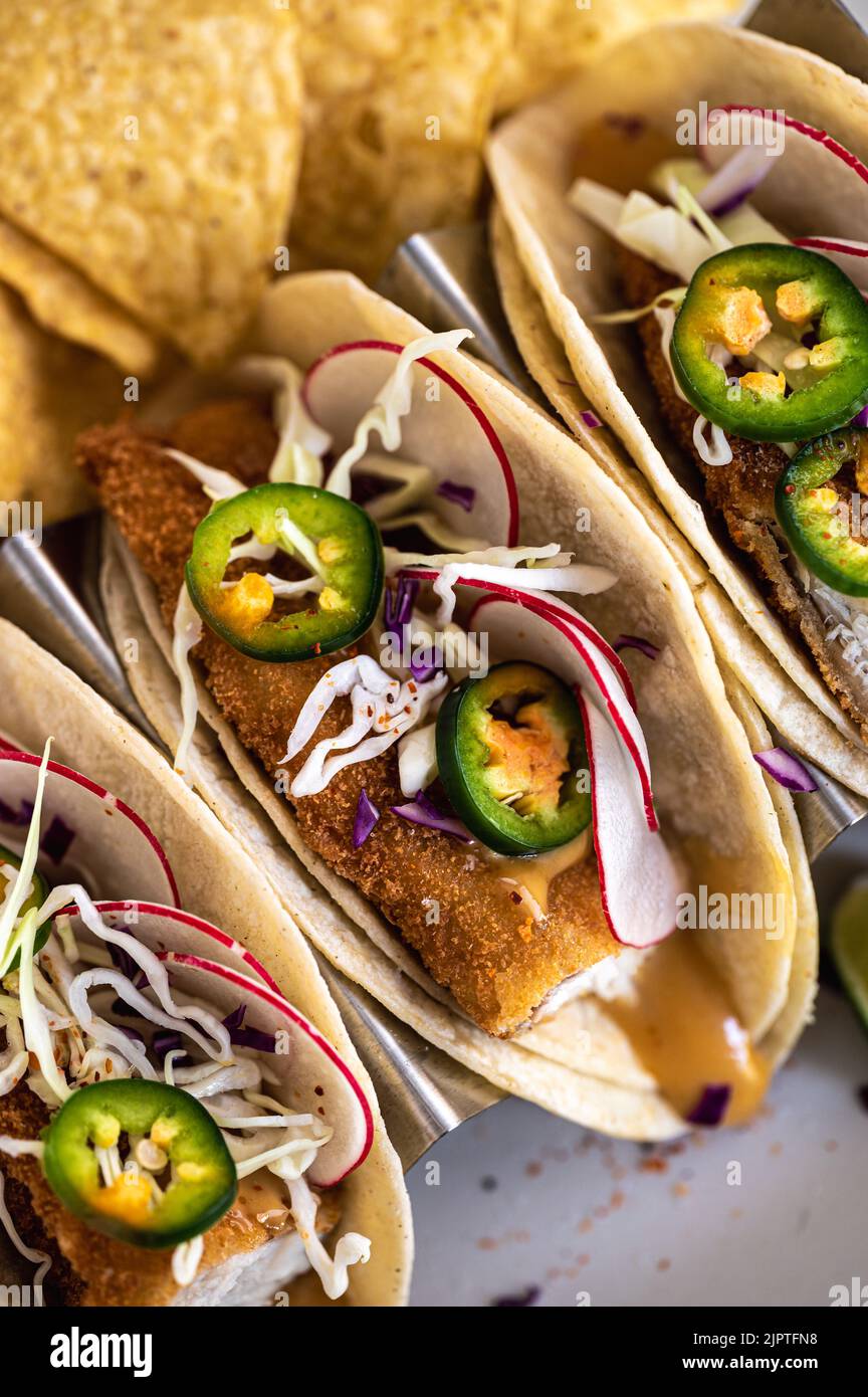The vertical view of crispy fish tacos with jalapenos, radishes, and