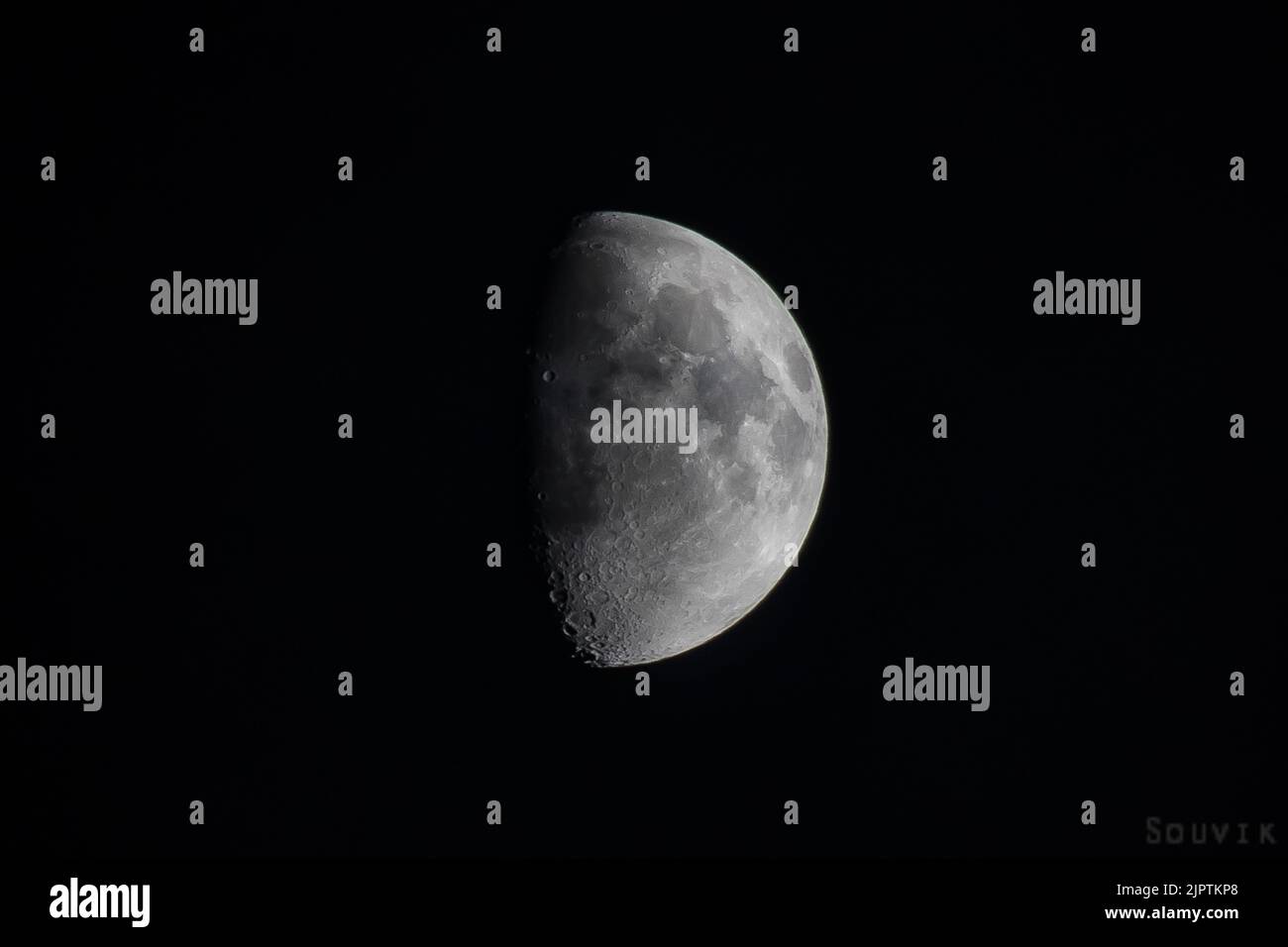 half moon with moon craters and patches visible. shot against dark black sky. Stock Photo