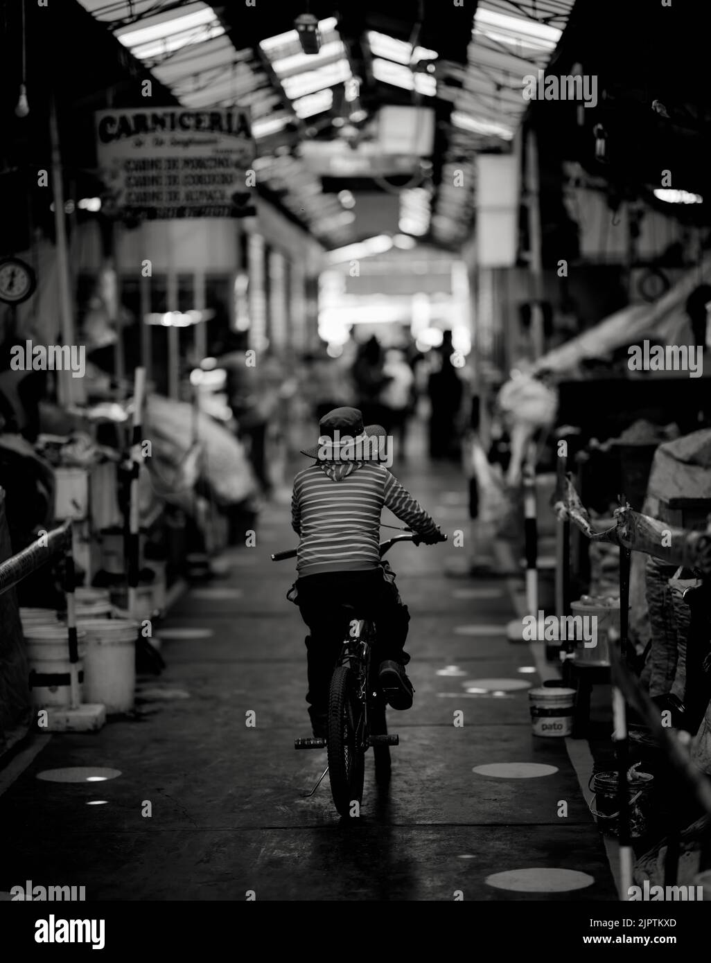 A vertical grayscale shot of a kid on a cycle in a street market in ...