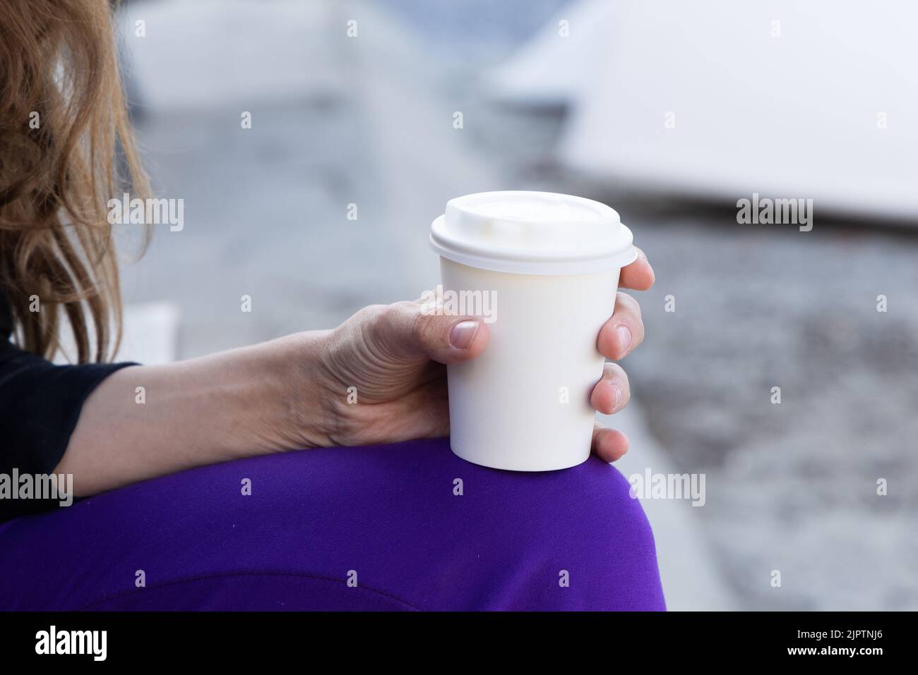 Young woman holds a disposable cup of coffee on on a sunny morning at the beach. Take away coffee at the sea. Stock Photo
