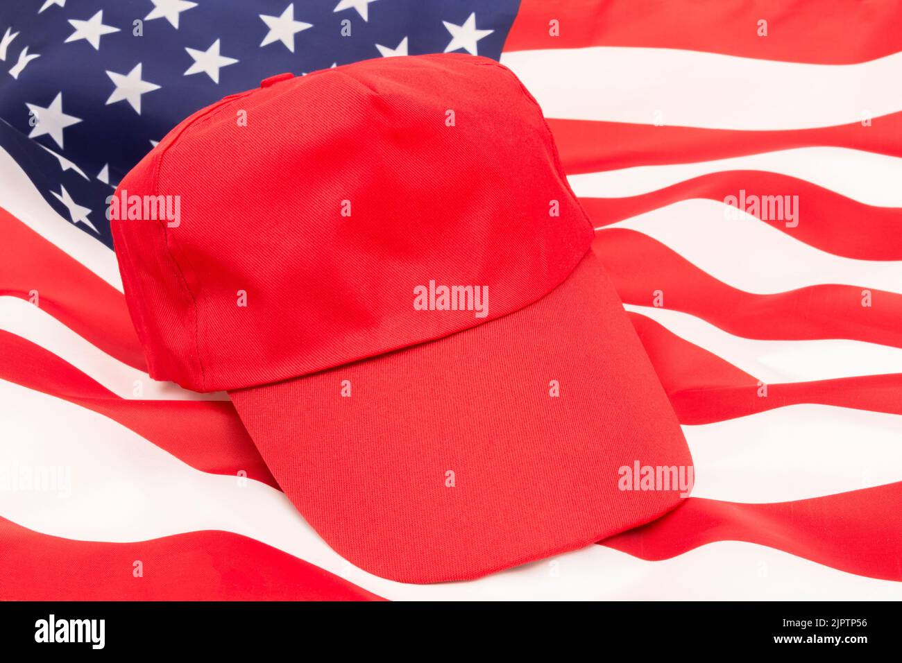 Red MAGA-type hat with blank caption area on US Stars and Stripes flag. For Republicans 2024 Presidential elections, American elections, US red wave. Stock Photo