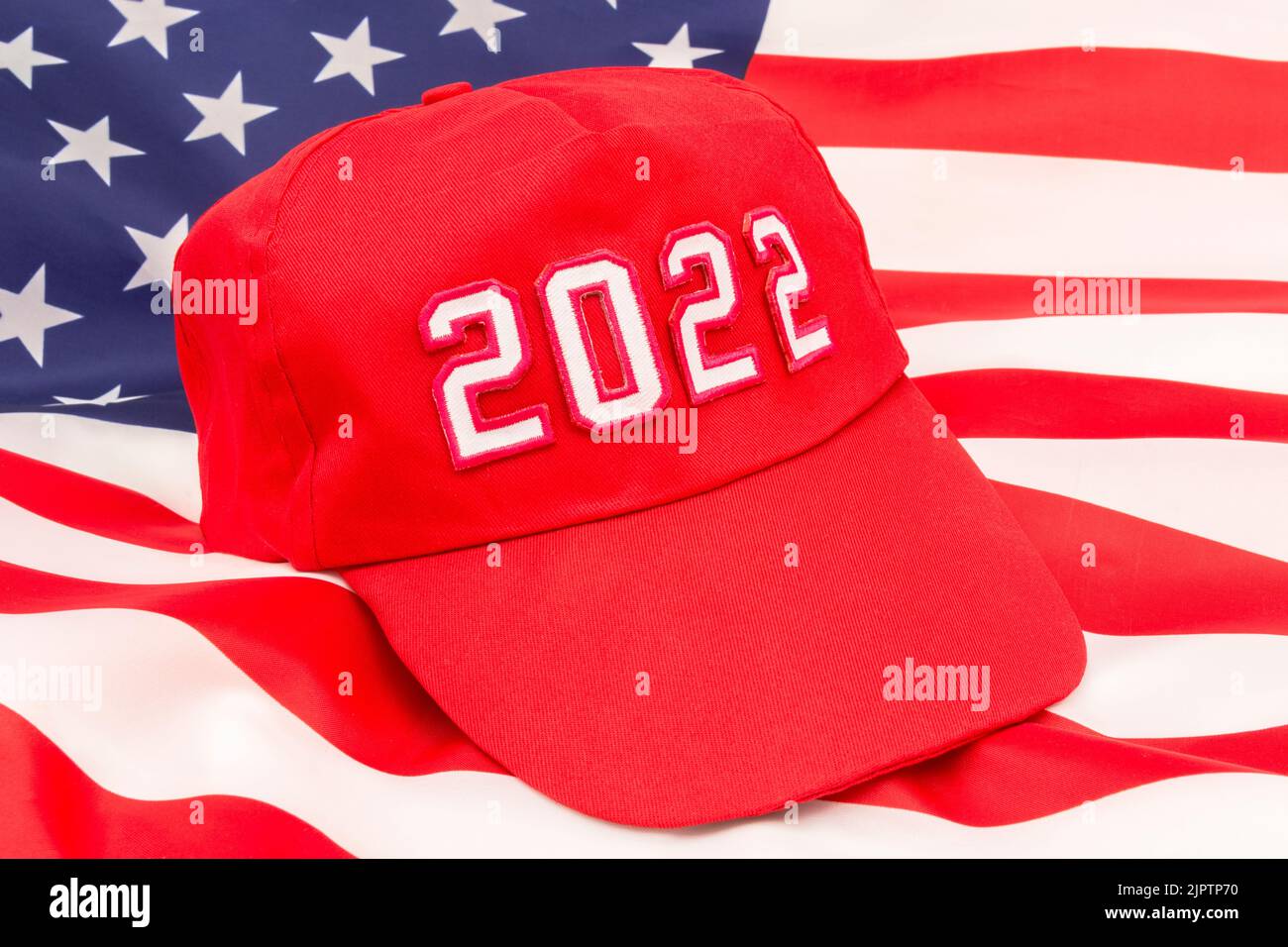 Red MAGA-type hat with 2022 on backdrop US Stars and Stripes flag. For Republican wins in 2022 US Midterm elections in November & Republican Red Wave. Stock Photo