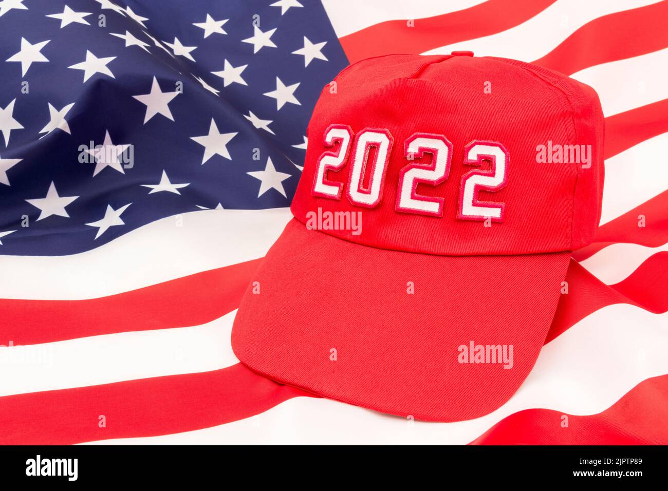 Red MAGA-type hat with 2022 on backdrop US Stars and Stripes flag. For Republican wins in 2022 US Midterm elections in November & Republican Red Wave. Stock Photo
