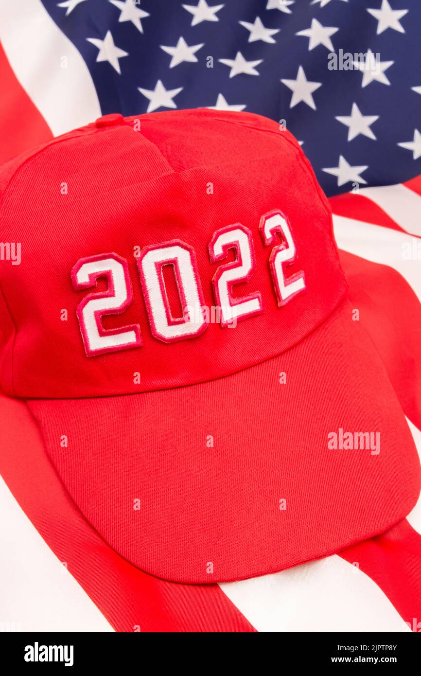 Red MAGA-type hat with 2022 on backdrop US Stars and Stripes flag. For Republican wins in 2022 US Midterm elections in November & Republican Red Wave. Stock Photo
