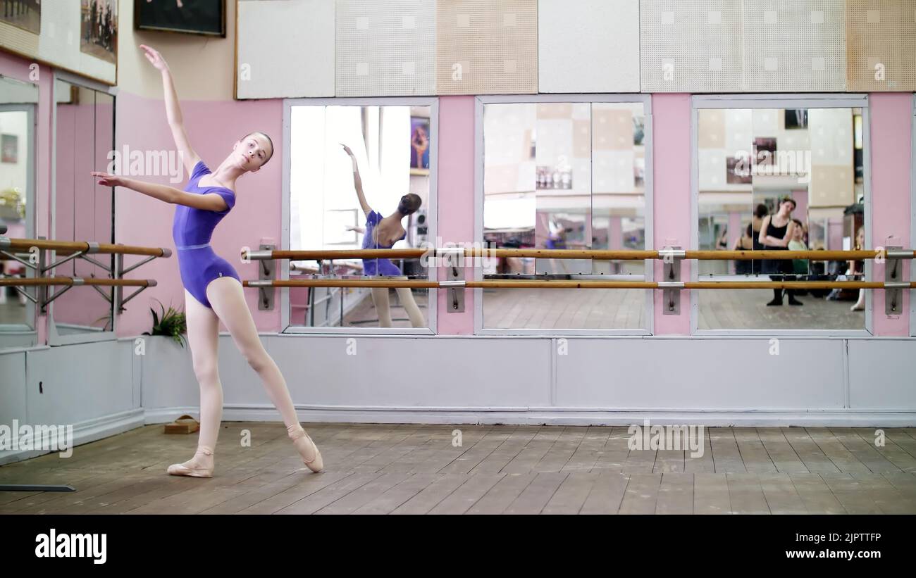 in dancing hall, Young ballerina in purple leotard performs tour chenne on pointe shoes, moves with turns elegantly, at mirror in ballet class. High quality photo Stock Photo