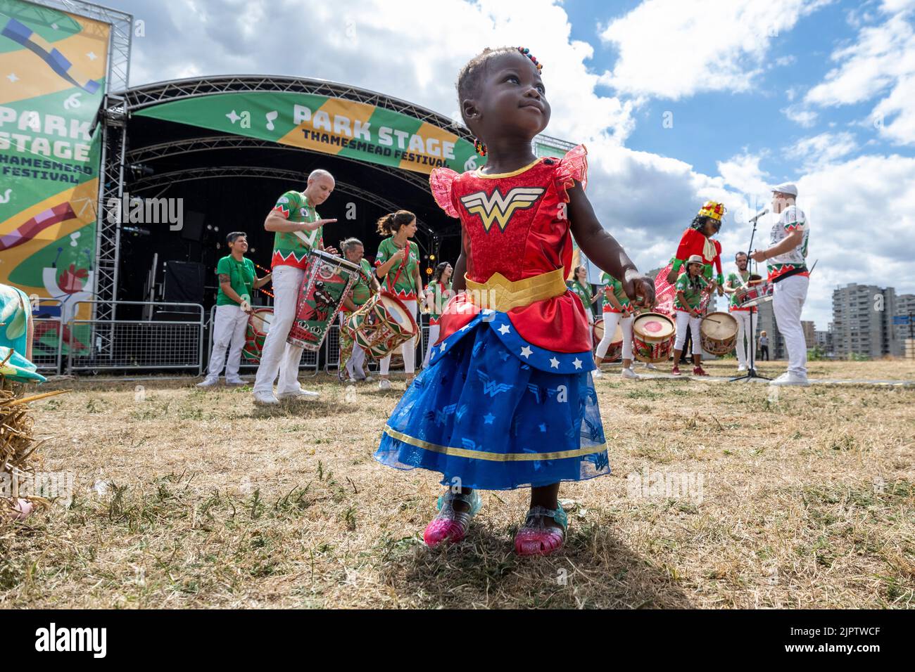 London, UK.  20 August 2022. A young visitor dressed as Wonder Woman watches members of the Taru Arts samba drumming group perform at the Thamesmead Festival in south east London.  Organised by a dedicated group of residents, it is the flagship community event each summer, showcasing singers, musicians and other creative home-grown Thamesmead talent. [Permission obtained]  Credit: Stephen Chung / Alamy Live News Stock Photo