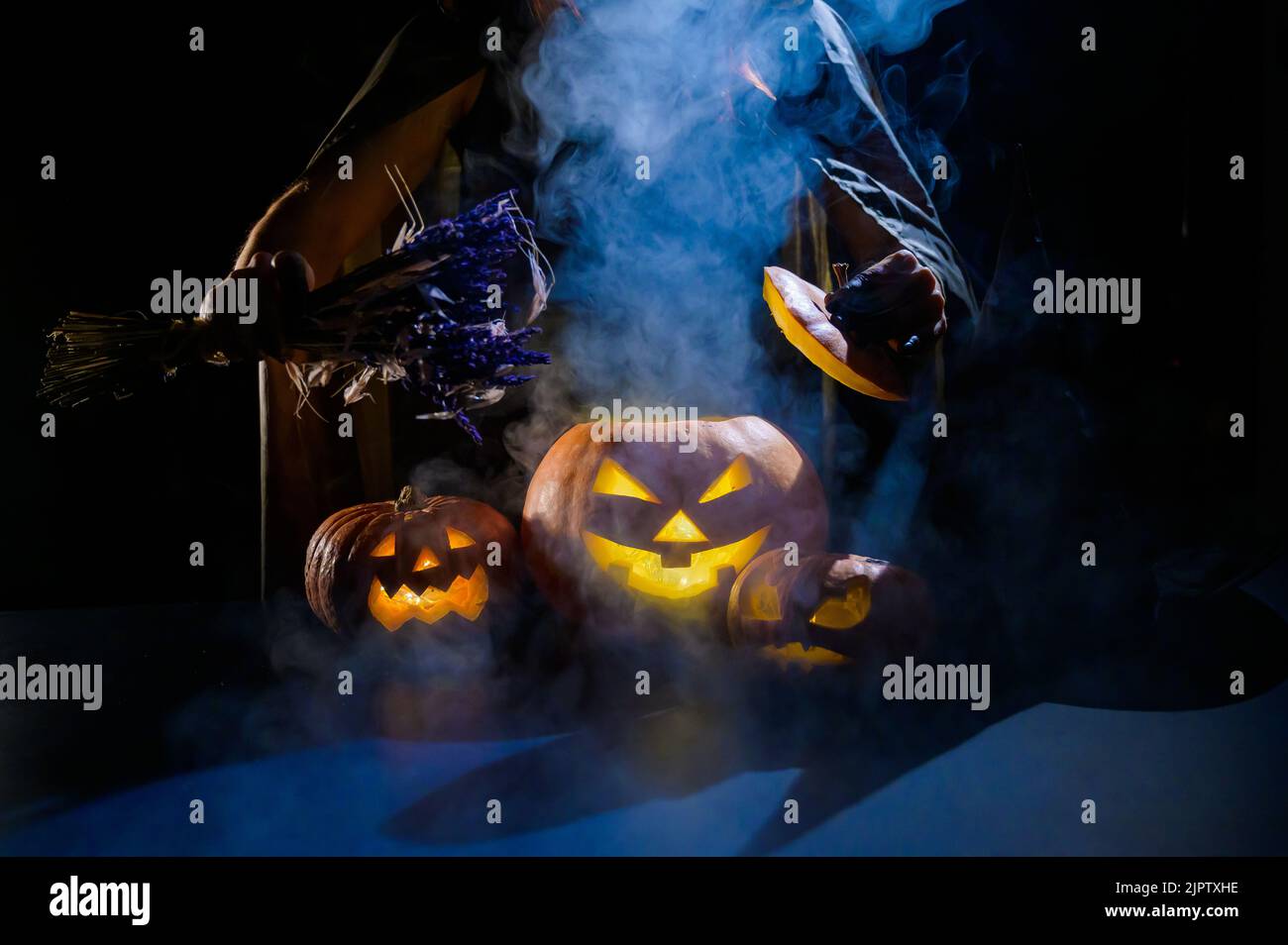 Witch casts a spell on a steaming pumpkin in the dark on Halloween ...