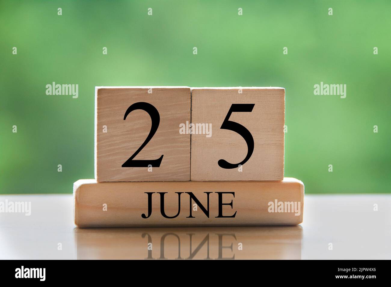 June 25 calendar date text on wooden blocks with blurred nature
